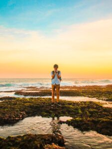 man standing on rocks near beach during golden hour