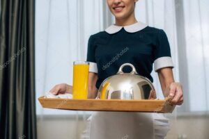 cropped shot of smiling maid in uniform holding breakfast covered with cloche on tray