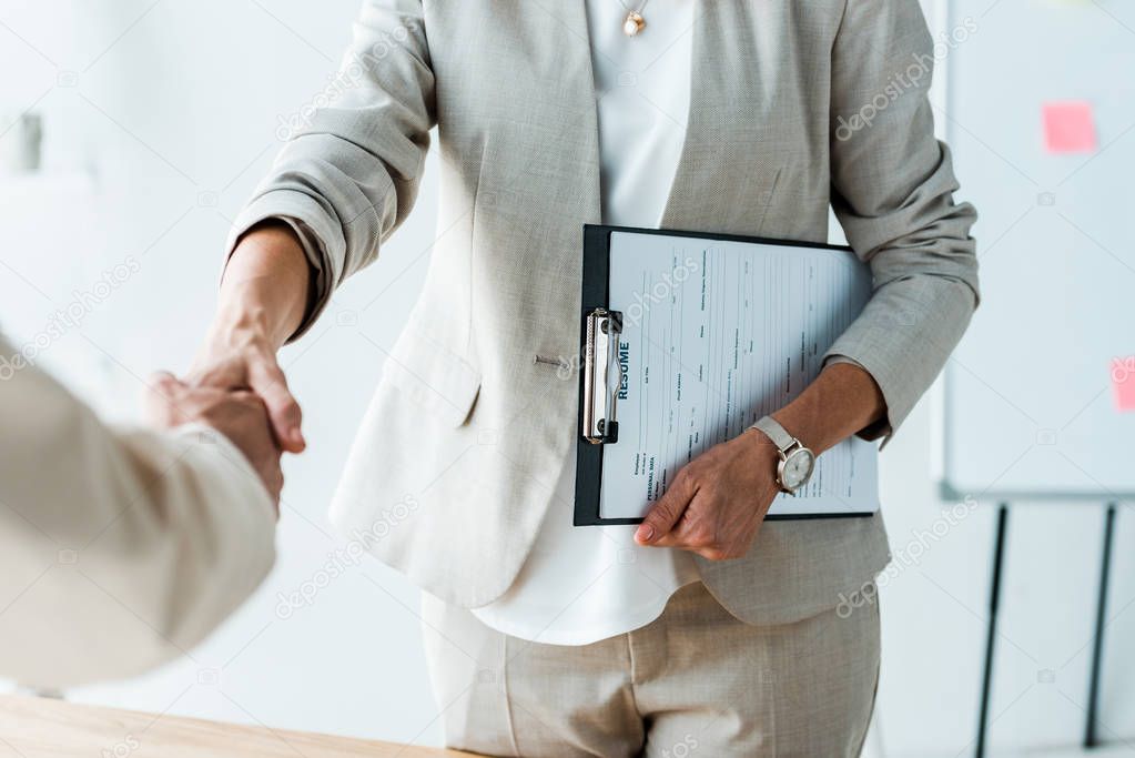 cropped view of recruiter and employee shaking hands in office