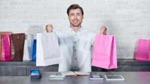 handsome young salesman holding shopping bags and smiling at camera in shop