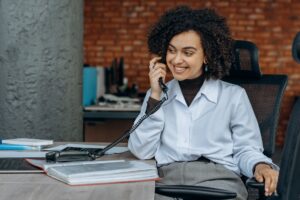 woman in white long sleeve shirt sitting on chair while talking on phone