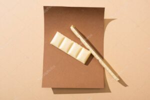 top view of delicious white chocolate bar pieces on paper on beige background