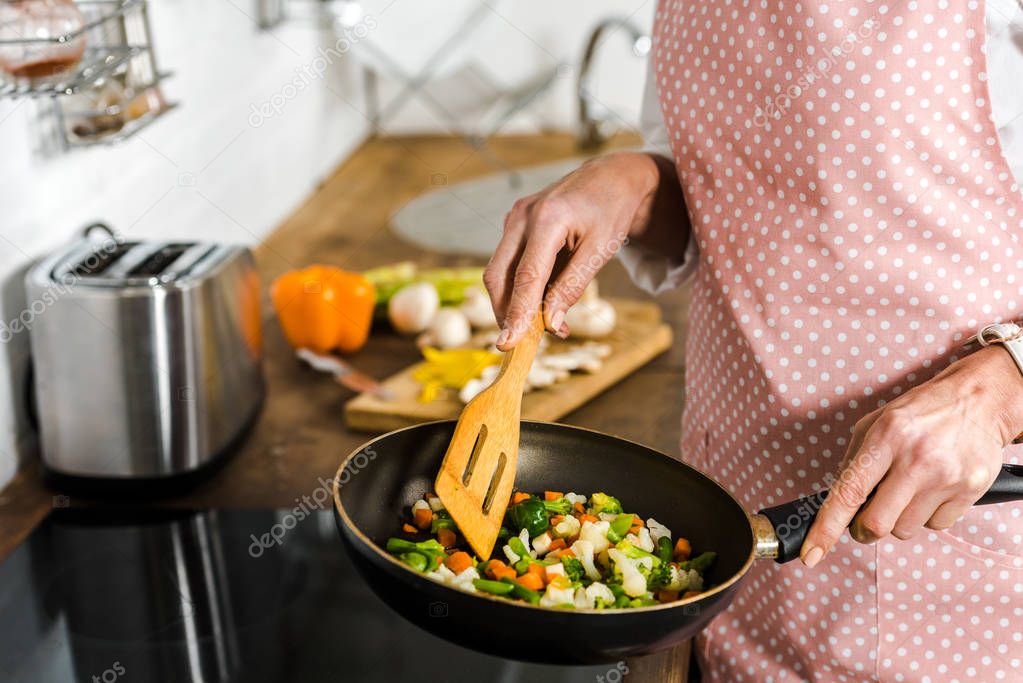 cropped image of mature woman frying vegetables in kitchen