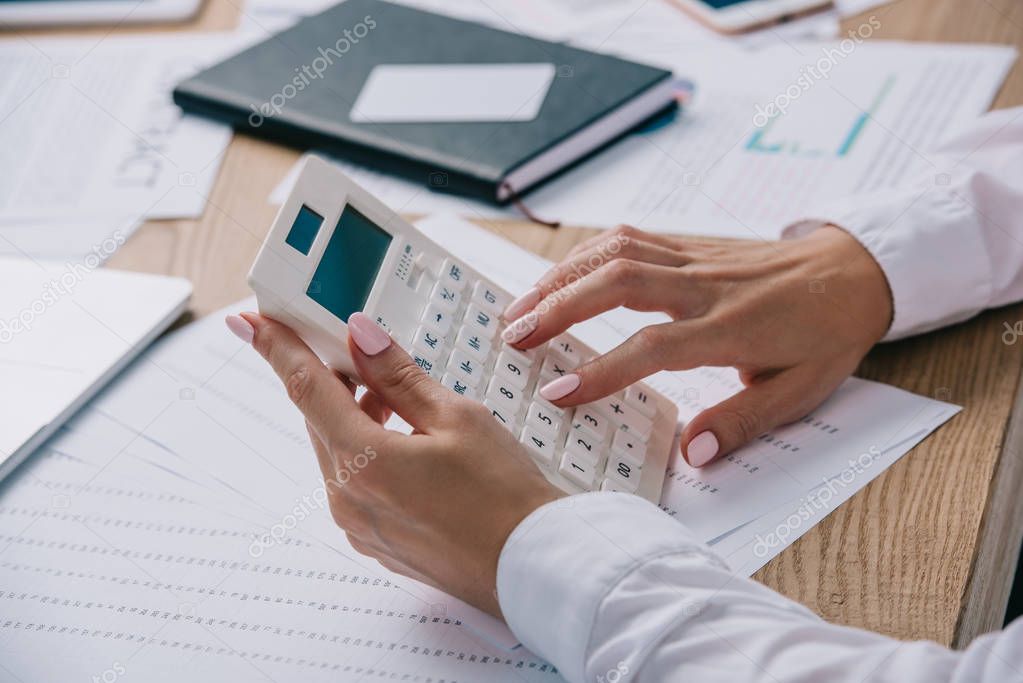 cropped shot of businesswoman making calculations on calculator at workplace with documents