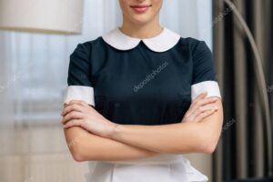 cropped shot of smiling maid in uniform with crossed arms