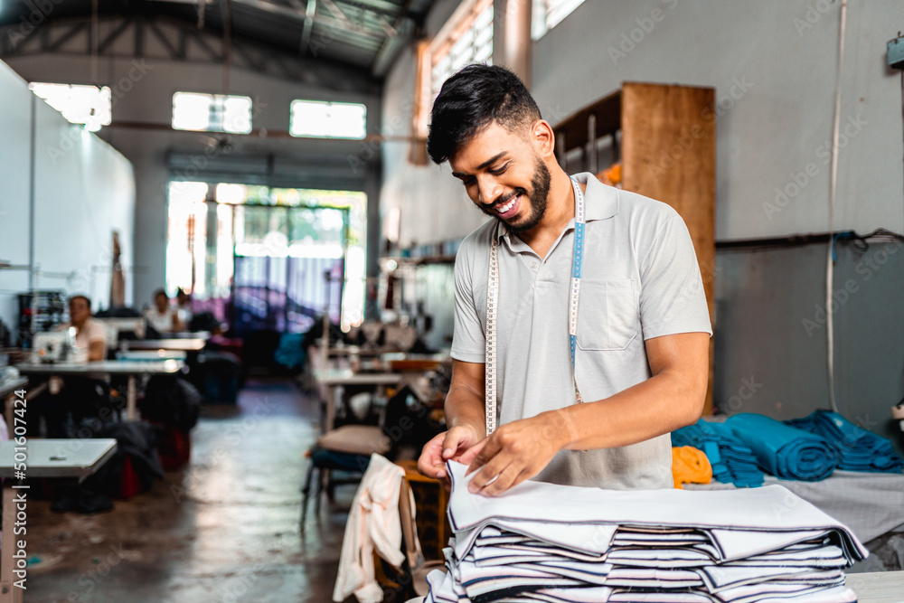 Rapaz sorridente conferindo as peças de tecido em um atelier