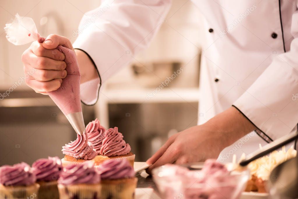 cropped shot of confectioner putting cream on cupcakes