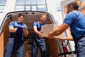 Low angle view of movers holding cardboard box near colleague writing on clipboard