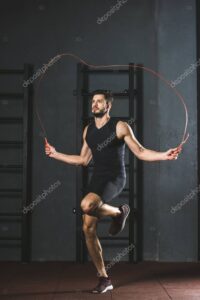 Young sportsman doing jump rope workout in gym
