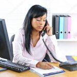 Serious black businesswoman on phone at desk