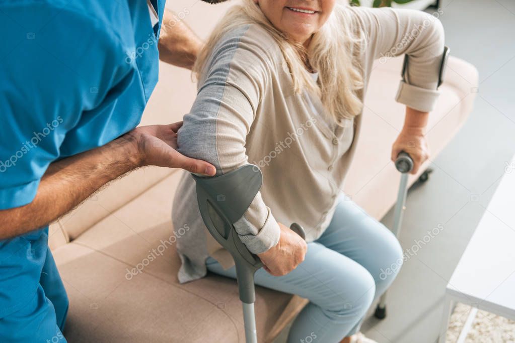 cropped shot of male nurse supporting senior woman with crutches