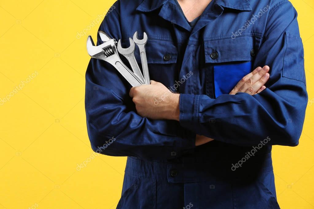Mechanic with crossed arms and wrench standing on yellow background