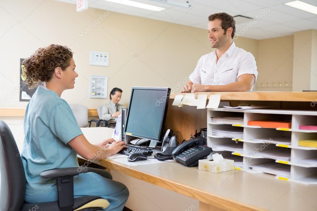 Nurse And Patient Conversing At Reception Desk