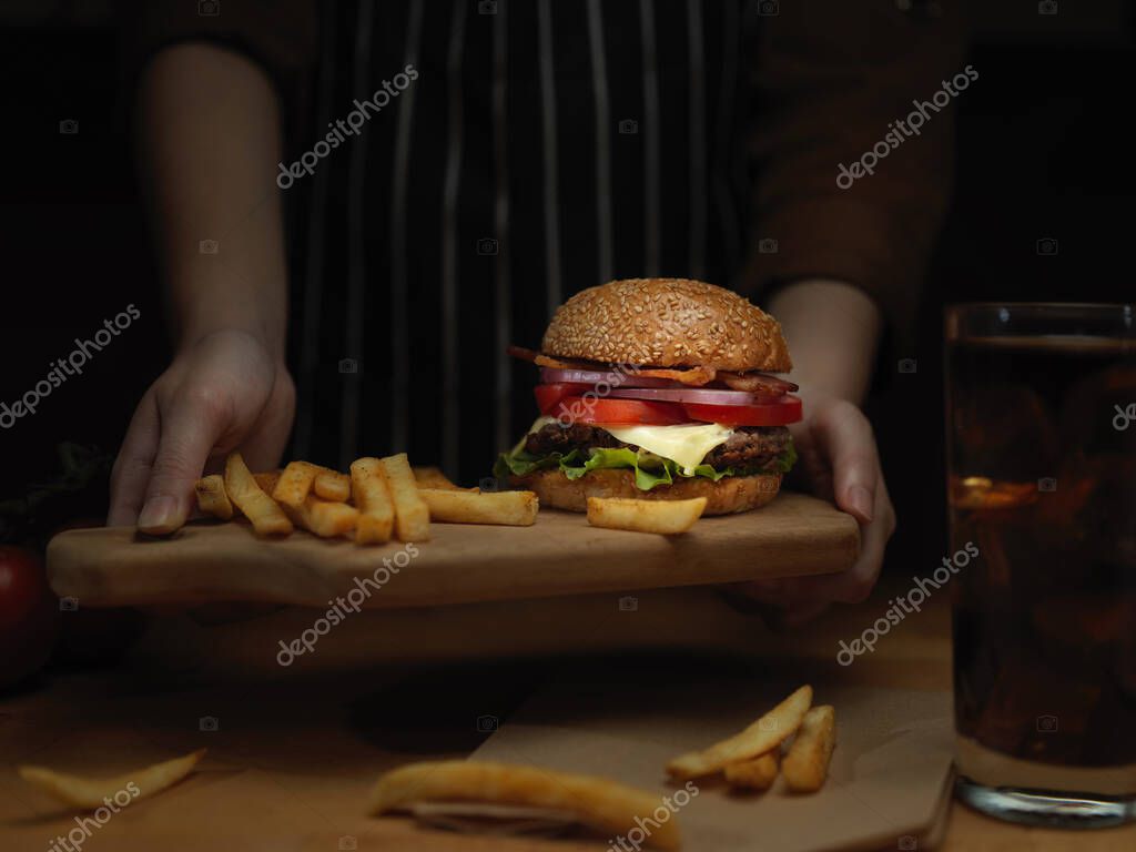 Close up view of female hands serving fresh tasty homemade burger with French fries and beverage in restaurant