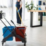 Selective focus of buckets with cleaning supplies and multiethnic cleaners working in office